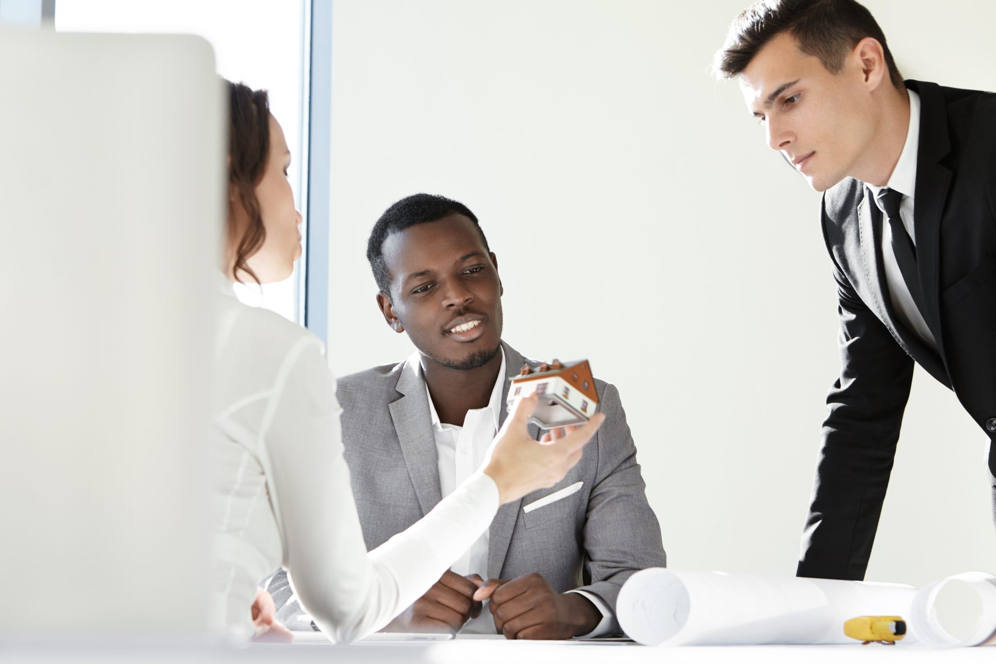 home, design and architecture concept. brunette female client holding scale model of her future house during meeting with contractors, discussing details of project, sitting at table with blueprints